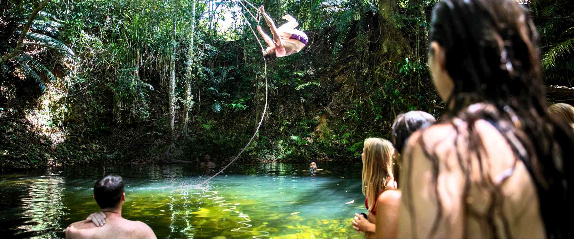 Man swinging from rope swing into natrual pool while others watch